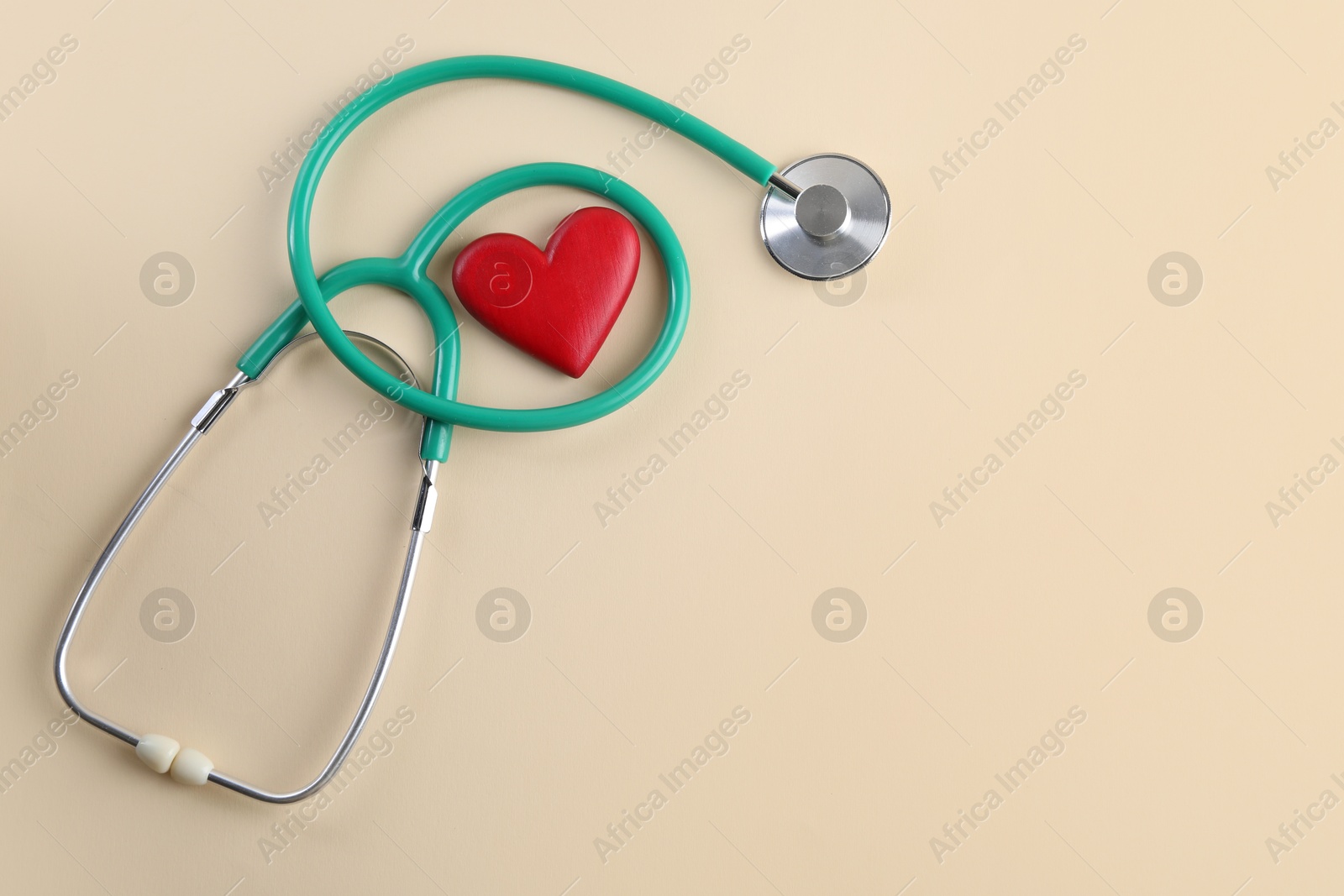 Photo of Stethoscope and red heart on beige background. Space for text