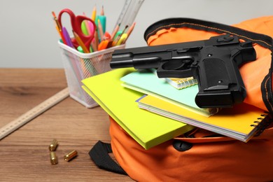 Photo of Gun, bullets and school stationery on wooden table , closeup