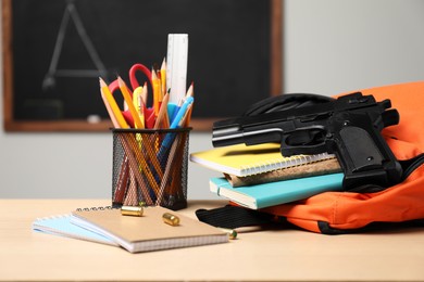 Photo of Gun, bullets and school stationery on wooden table indoors