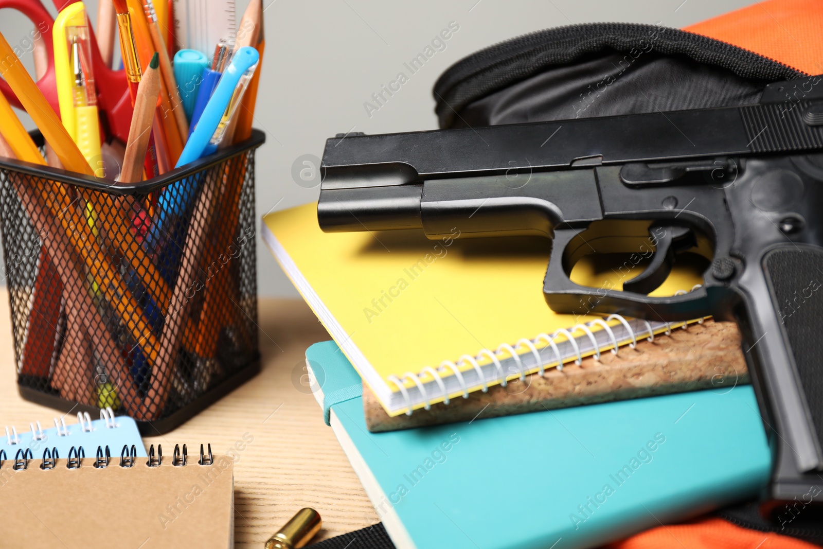 Photo of Gun, bullets and school stationery on wooden table, closeup