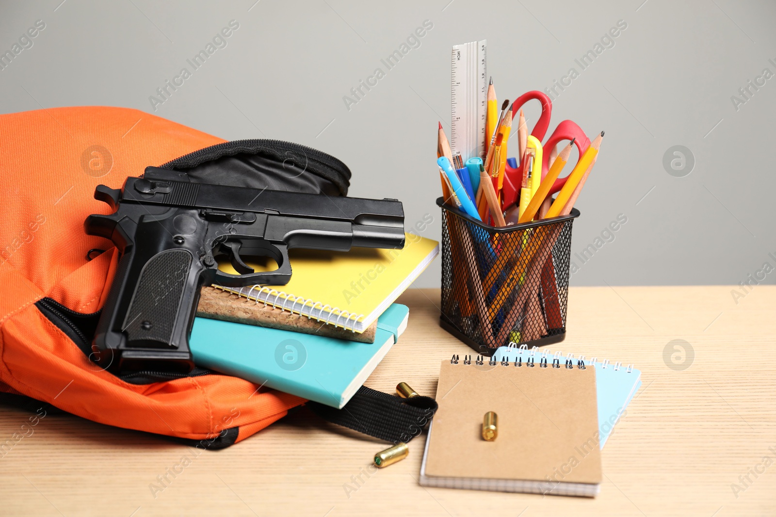 Photo of Gun, bullets and school stationery on wooden table