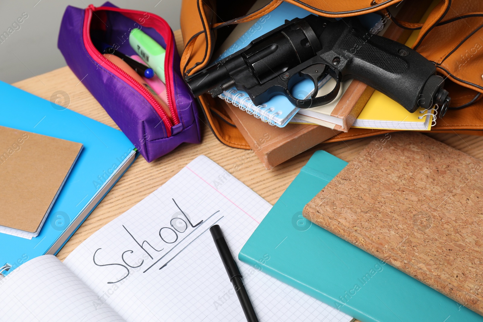 Photo of Gun and school stationery on wooden table, above view