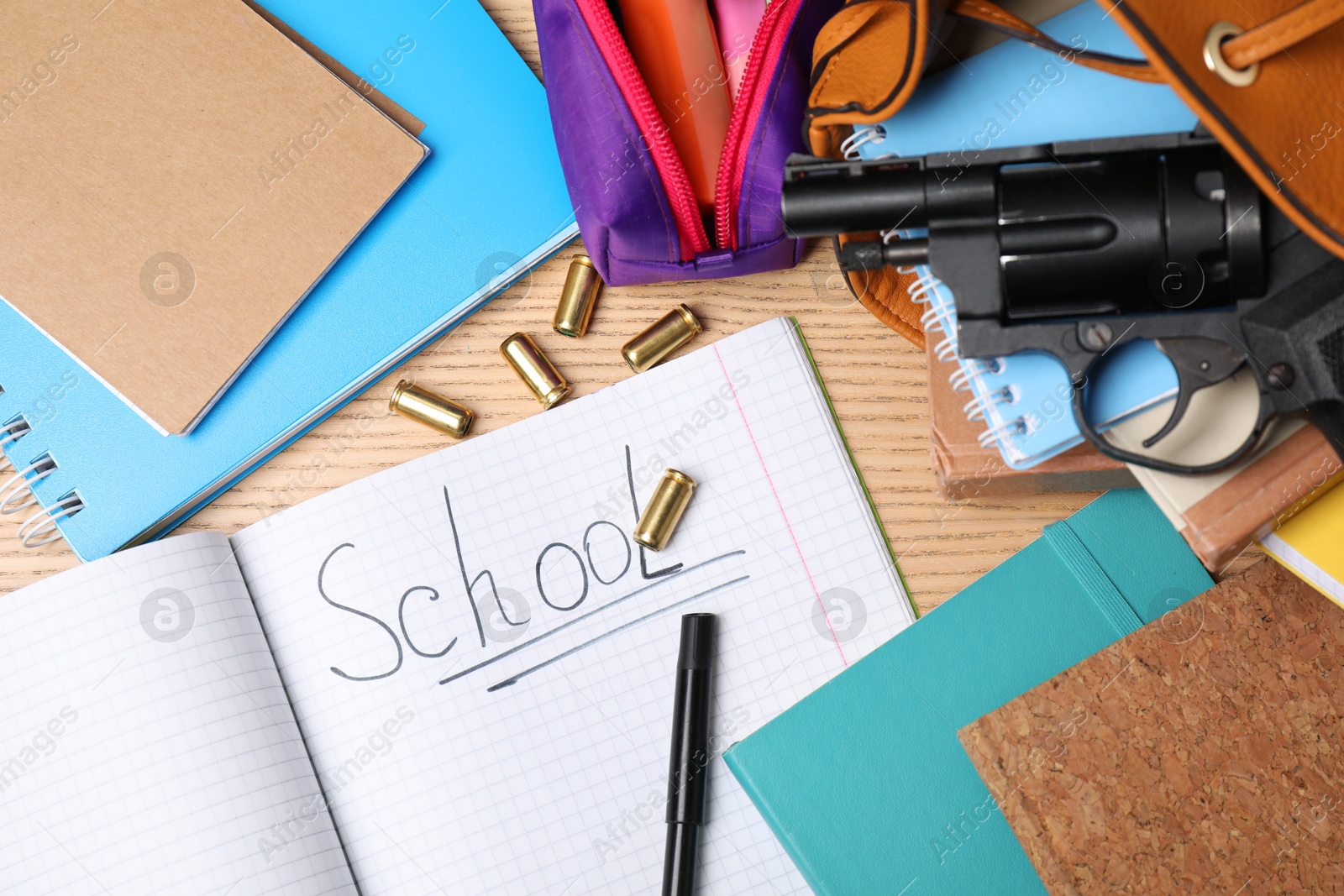 Photo of Gun, bullets and school stationery on wooden table, flat lay