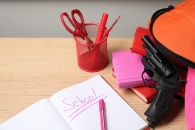 Photo of Gun and school stationery on wooden table, space for text