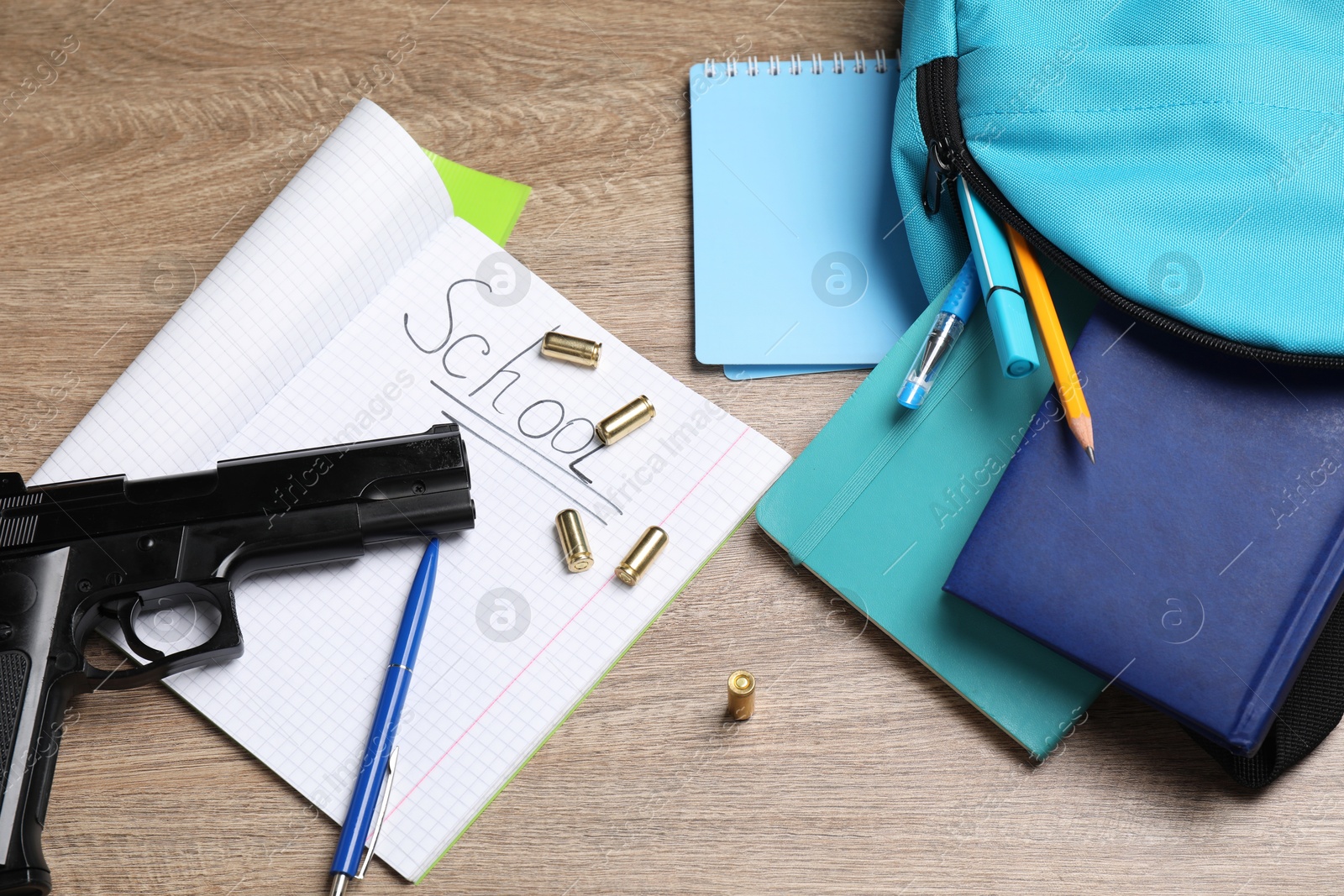 Photo of Gun, bullets and school stationery on wooden table, flat lay