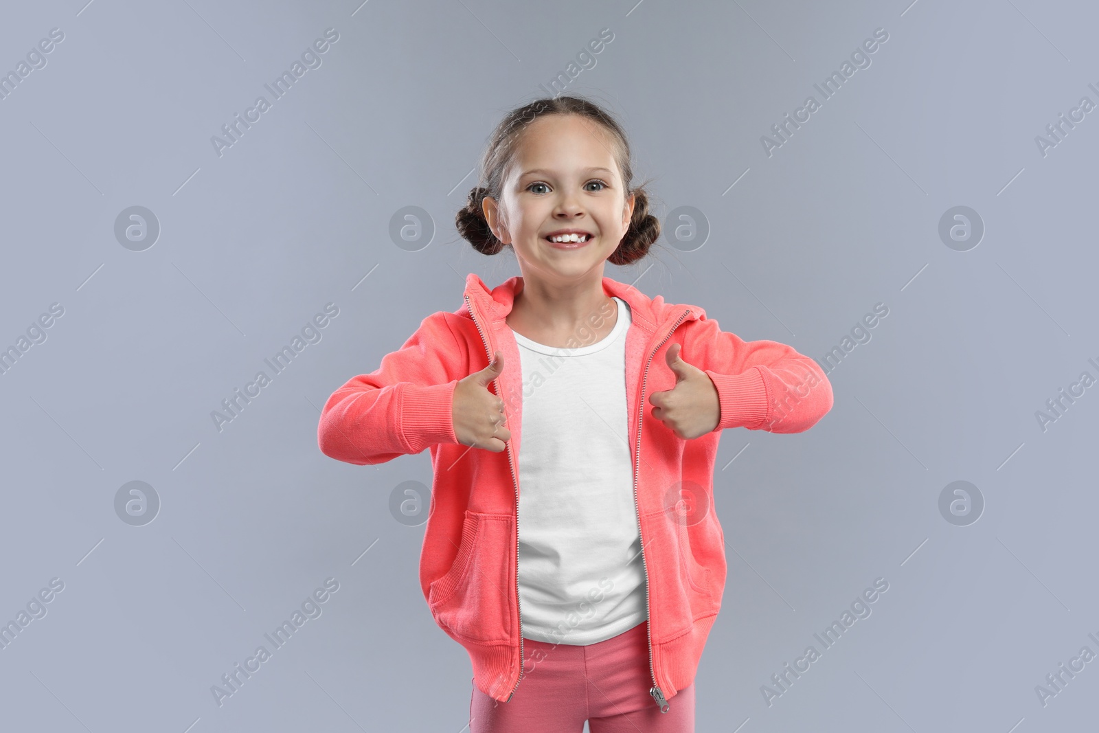 Photo of Cute little girl showing thumbs up on grey background