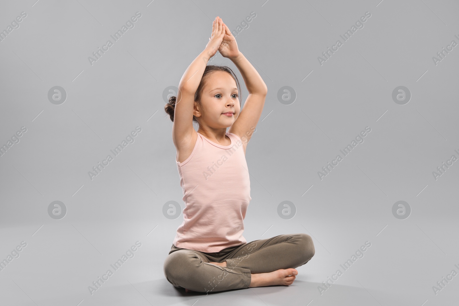 Photo of Cute little girl practicing yoga on grey background