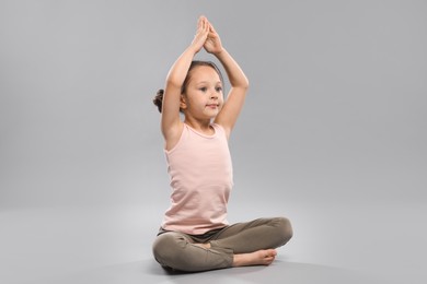 Photo of Cute little girl practicing yoga on grey background