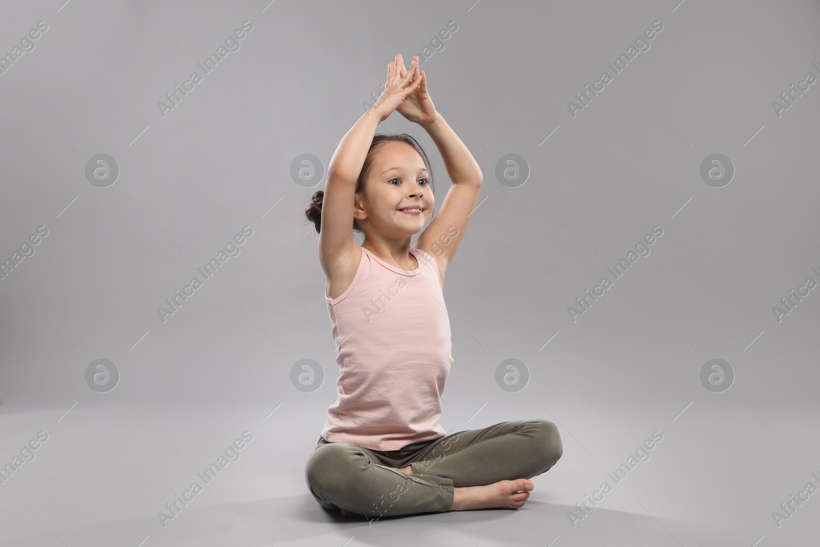 Photo of Cute little girl practicing yoga on grey background