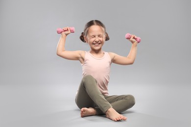 Photo of Cute little girl with dumbbells on grey background