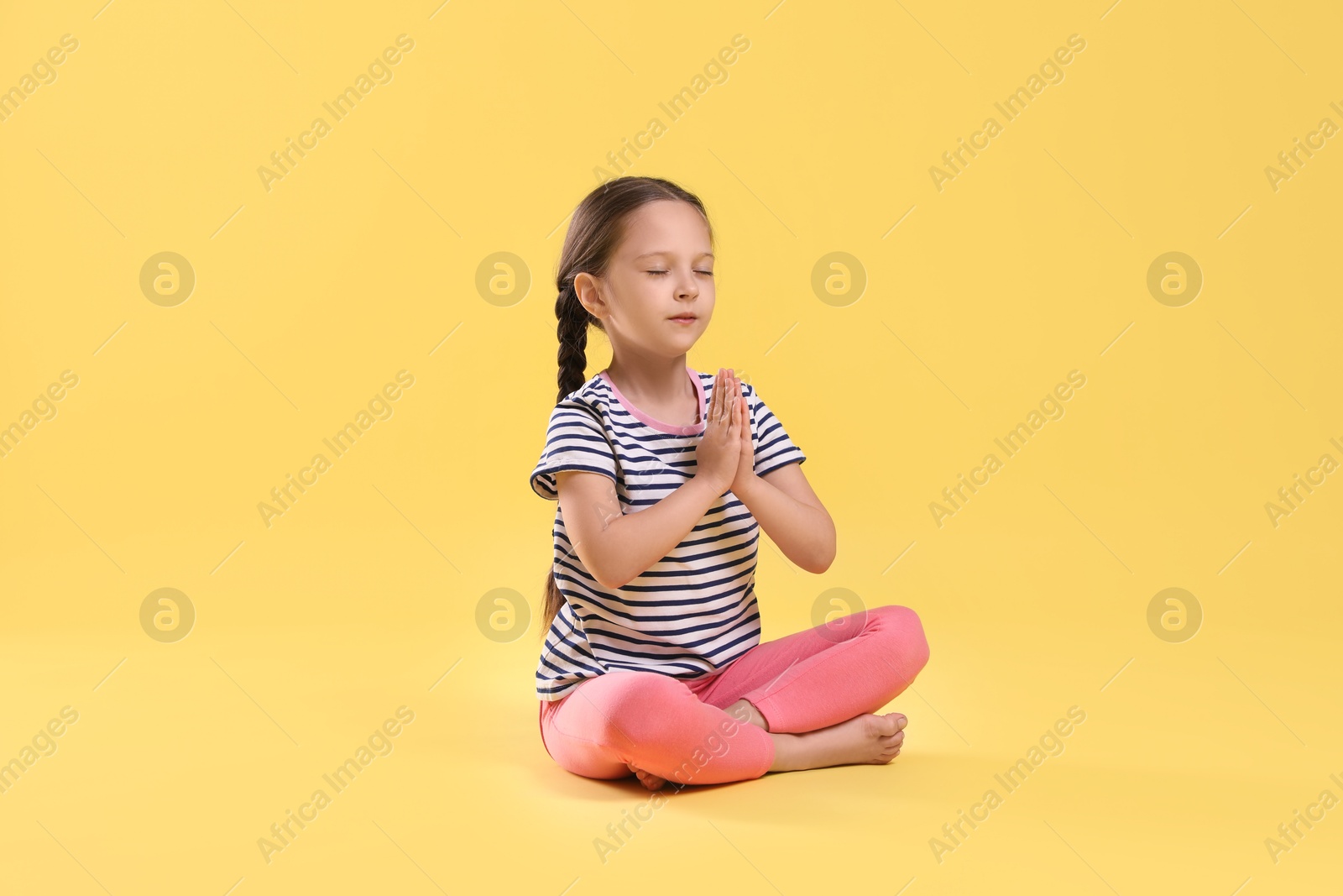 Photo of Cute little girl practicing yoga on yellow background