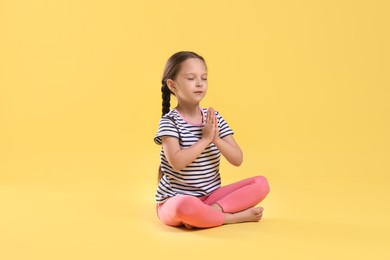 Photo of Cute little girl practicing yoga on yellow background