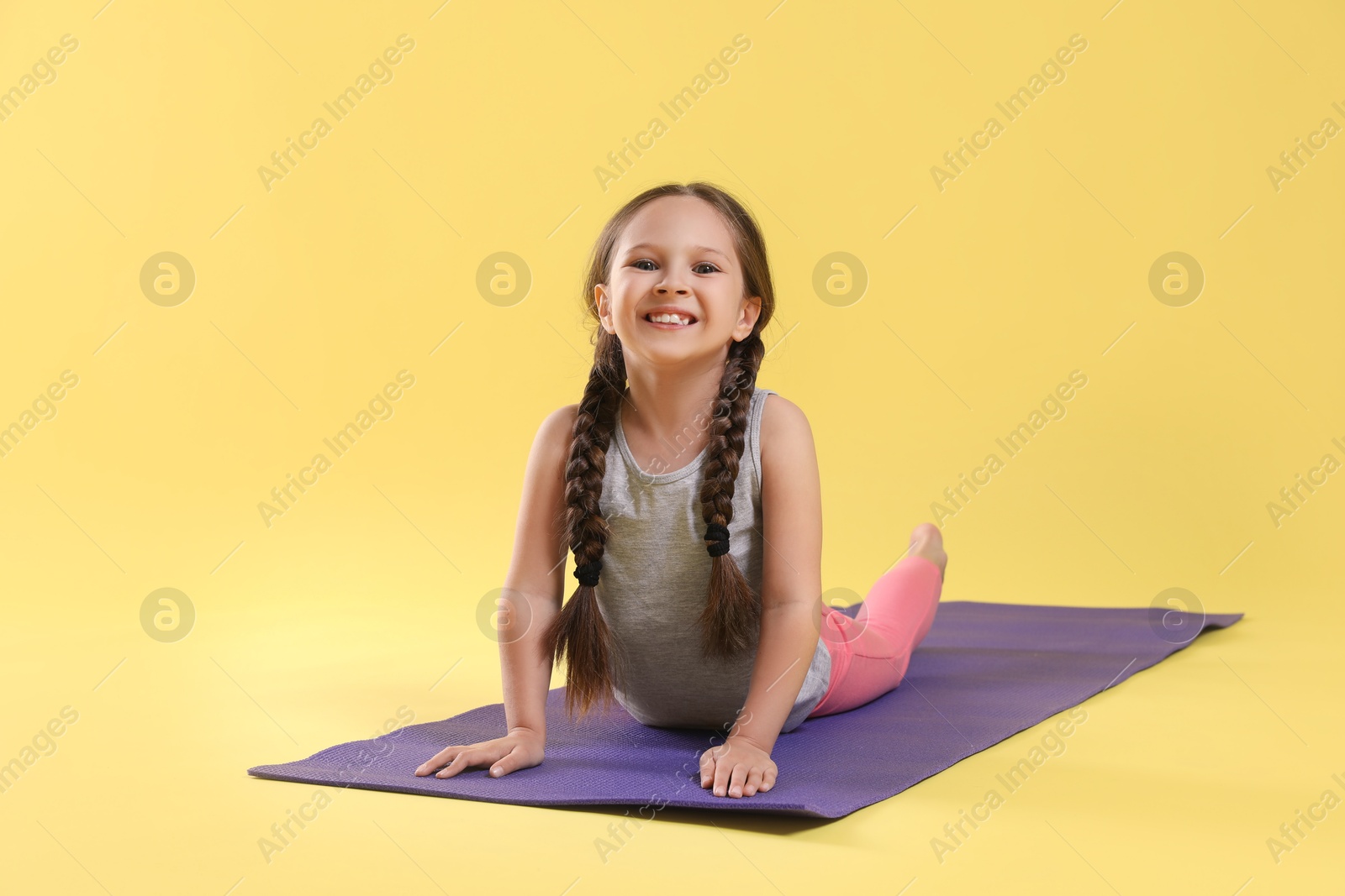 Photo of Cute little girl stretching on yellow background