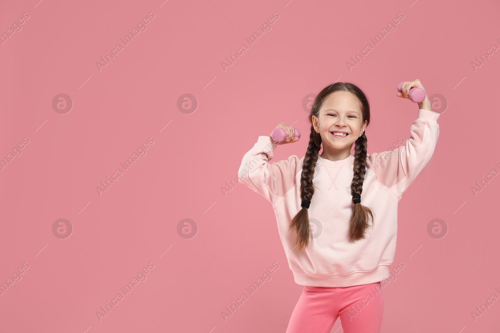 Photo of Cute little girl with dumbbells on pink background, space for text