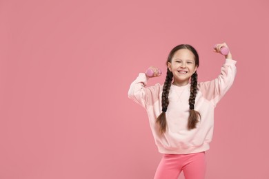 Cute little girl with dumbbells on pink background, space for text
