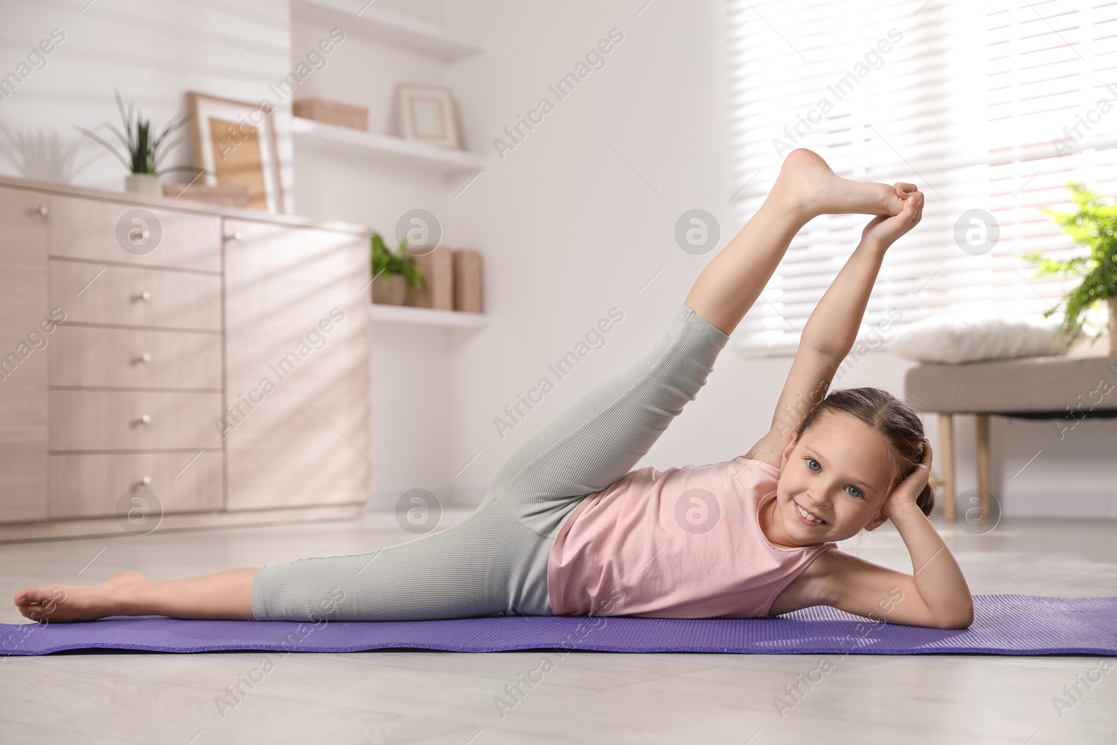 Photo of Cute little girl stretching herself on mat at home
