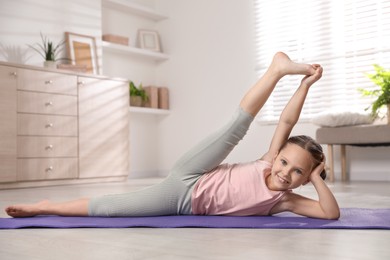 Photo of Cute little girl stretching herself on mat at home