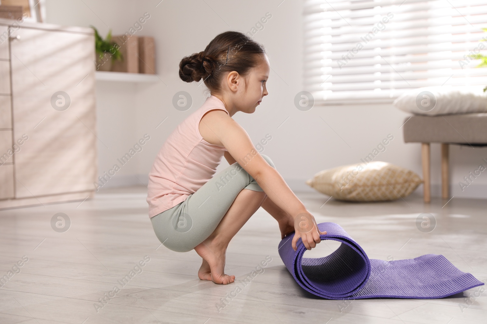 Photo of Cute little girl with fitness mat at home