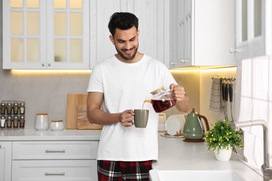 Morning of happy man pouring coffee from teapot into cup in kitchen