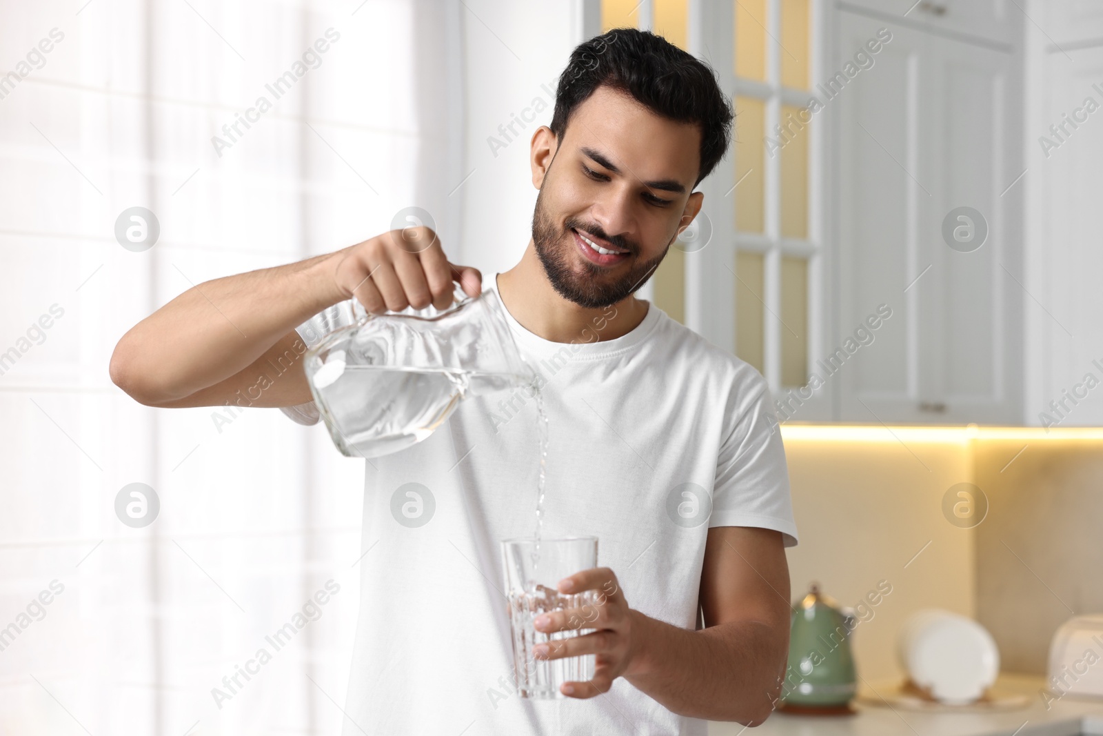 Photo of Morning of happy man pouring water from jug into glass in kitchen