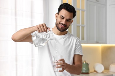 Morning of happy man pouring water from jug into glass in kitchen