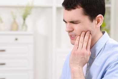 Man suffering from toothache at home, space for text