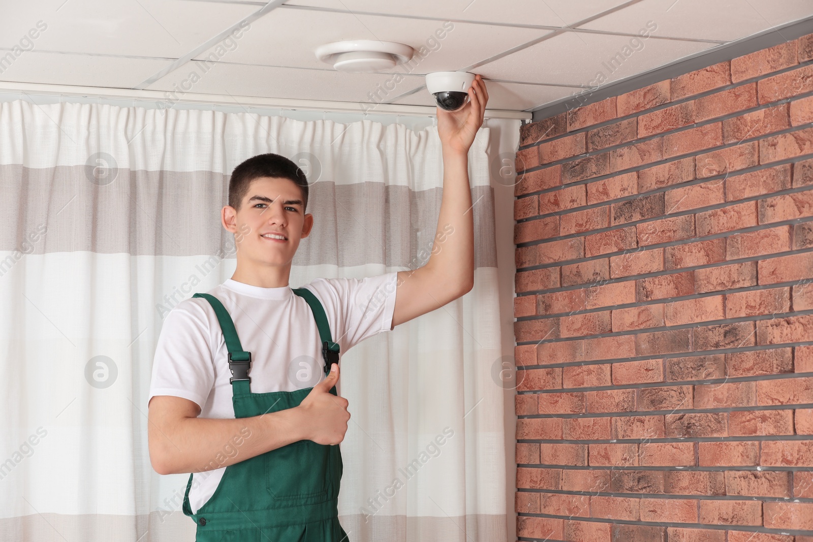 Photo of Technician showing thumbs up while installing CCTV camera on ceiling indoors