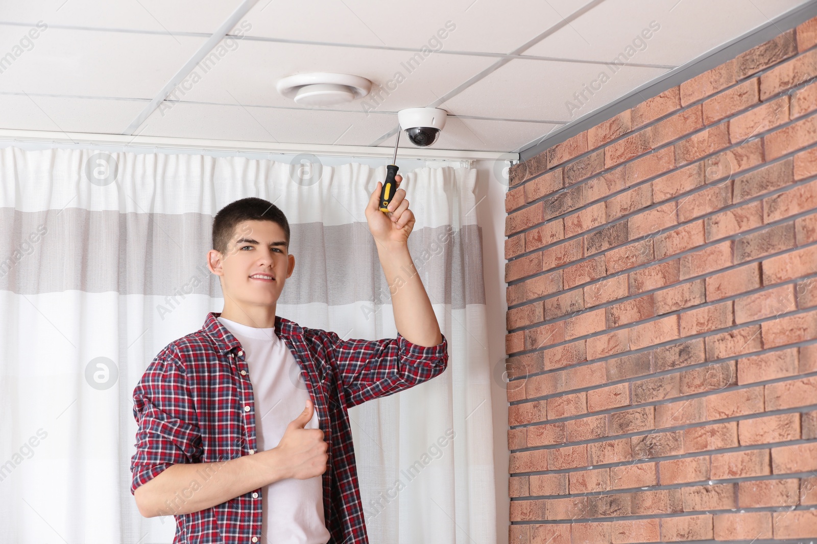 Photo of Technician showing thumbs up while installing CCTV camera with screwdriver on ceiling indoors