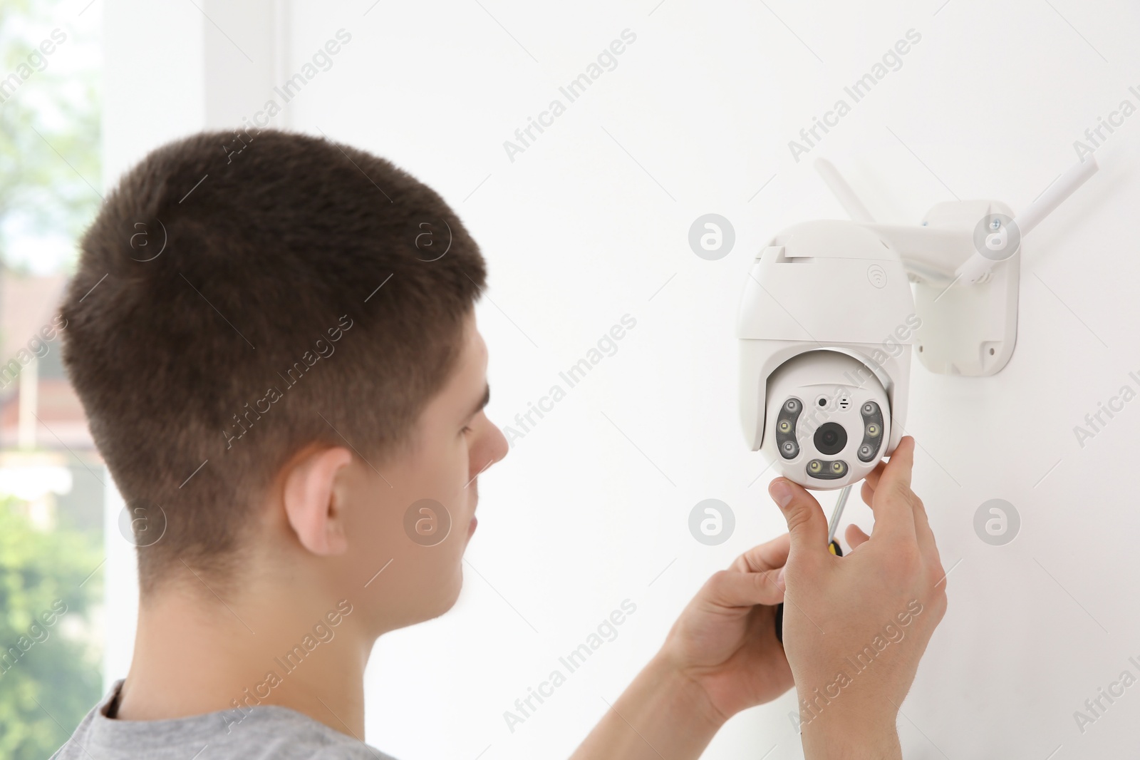 Photo of Technician with screwdriver installing CCTV camera on wall indoors