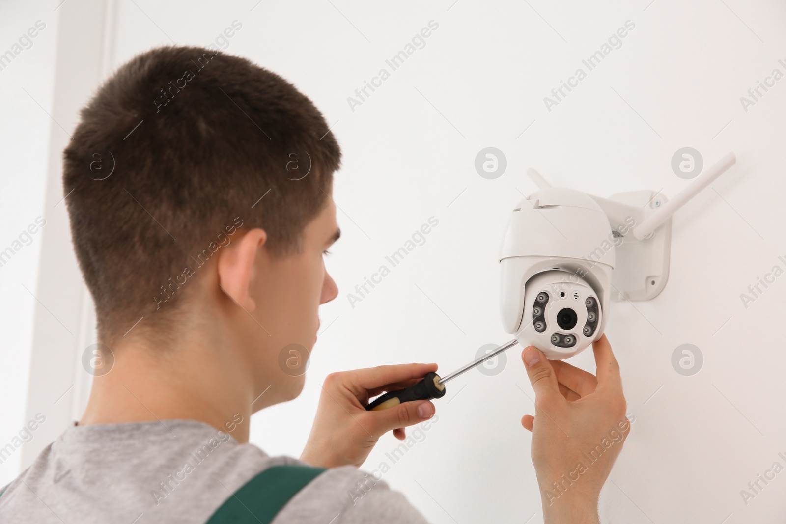 Photo of Technician with screwdriver installing CCTV camera on wall indoors