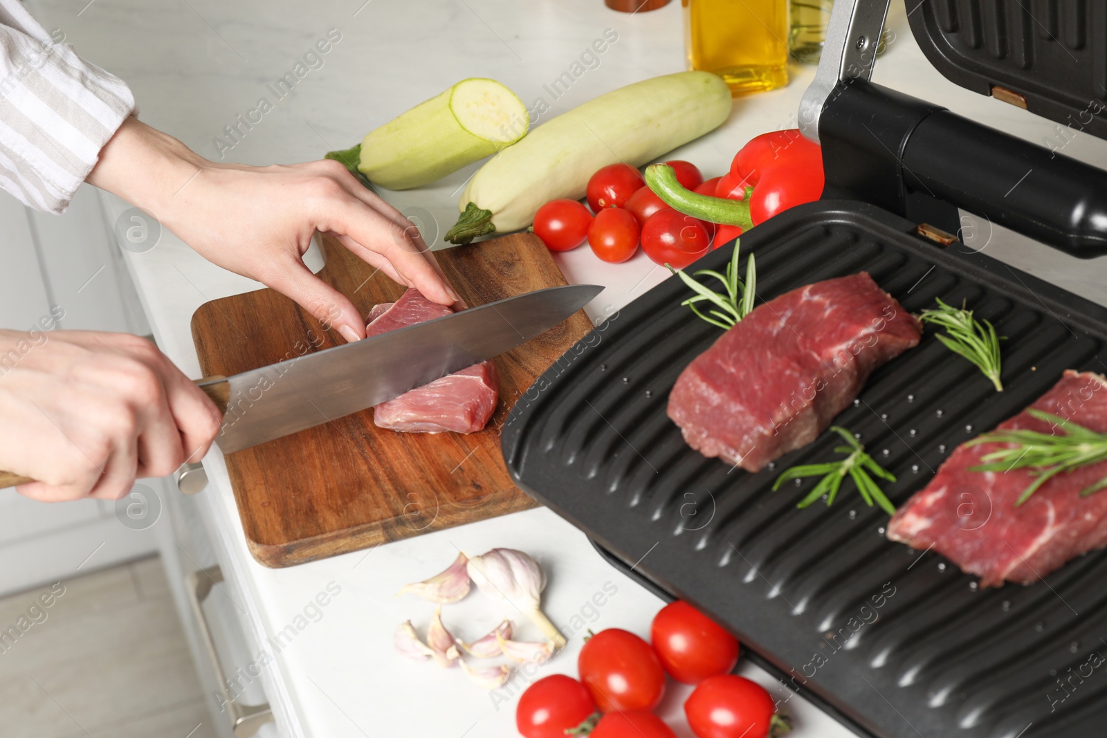 Photo of Woman cooking different products with electric grill at white wooden table in kitchen, closeup