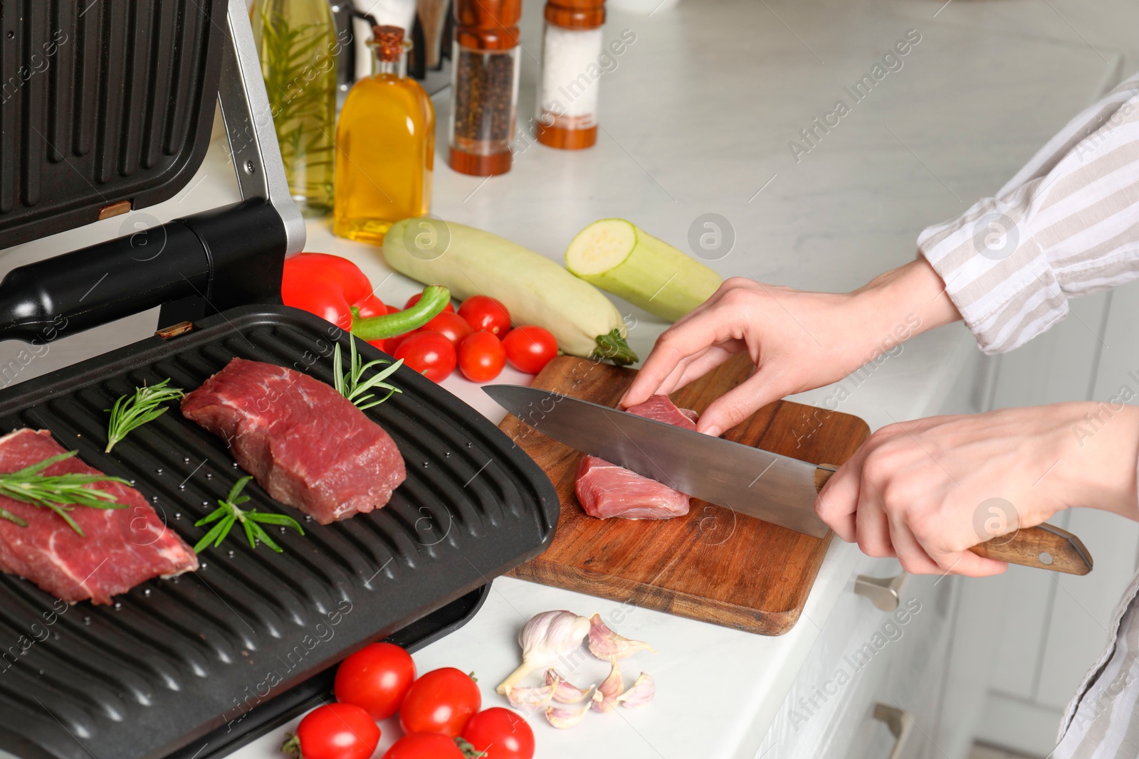 Photo of Woman cooking different products with electric grill at white wooden table in kitchen, closeup