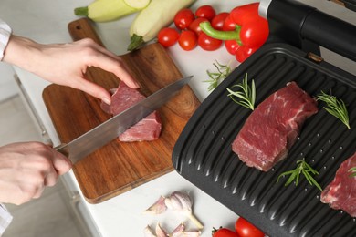 Woman cooking different products with electric grill at white wooden table in kitchen, above view