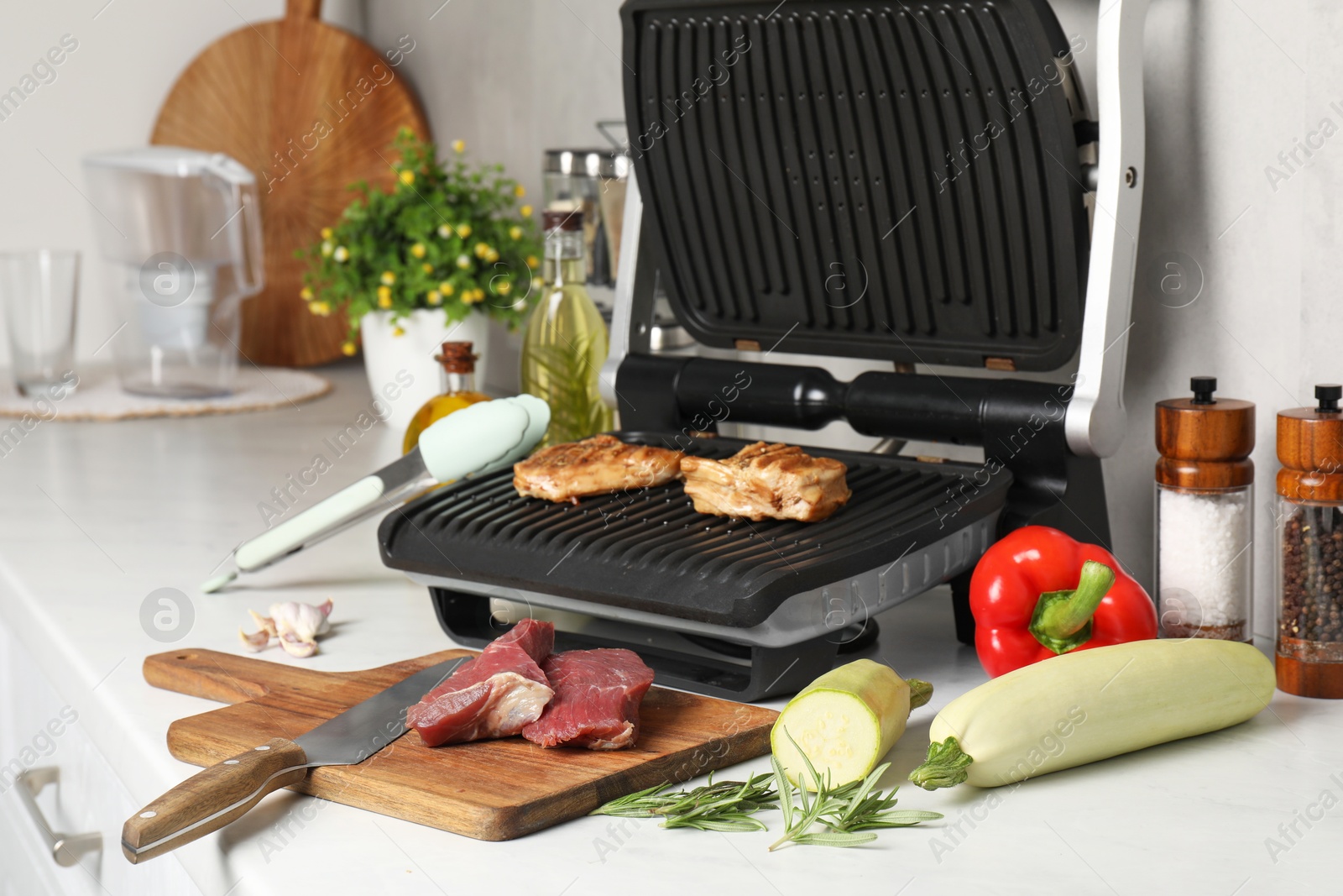 Photo of Electric grill and different products on white wooden table, closeup