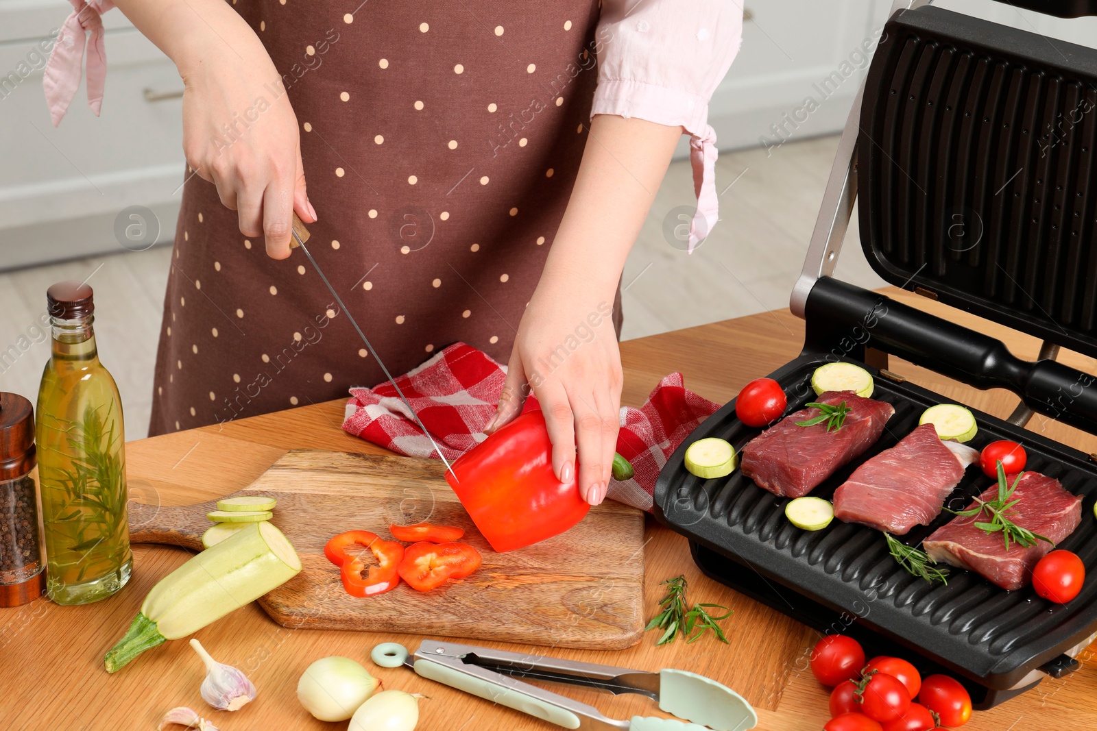 Photo of Woman cooking different products with electric grill at wooden table in kitchen, closeup