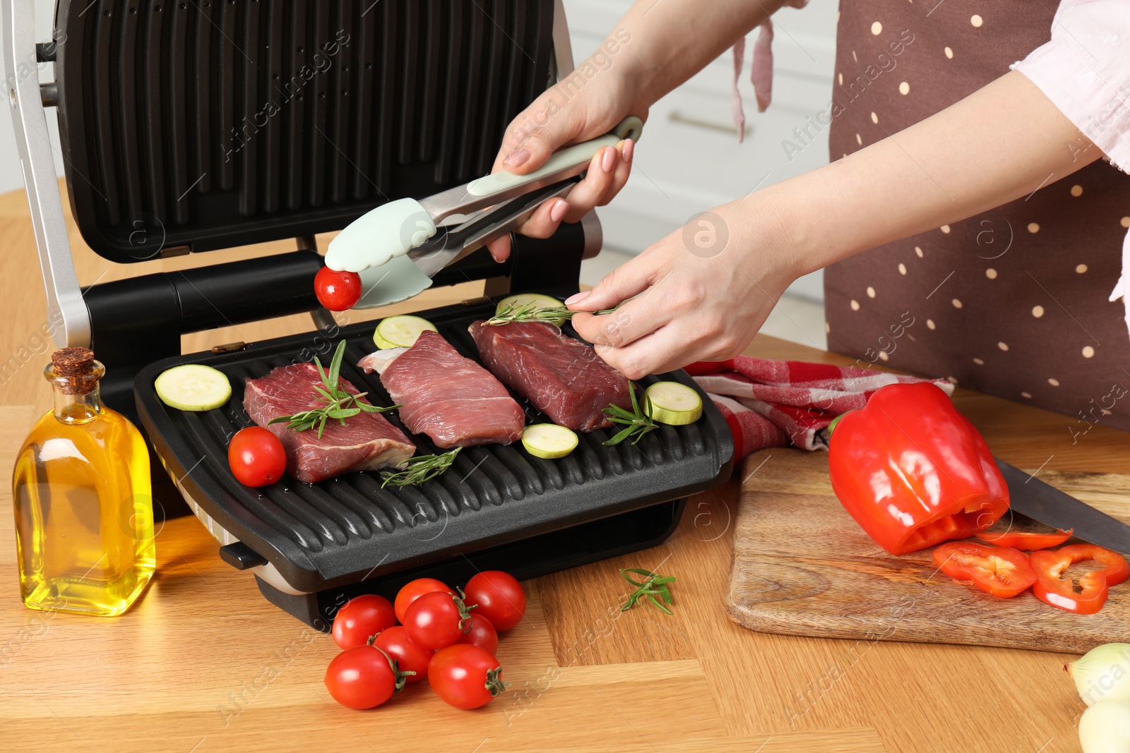 Photo of Woman cooking different products with electric grill at wooden table in kitchen, closeup