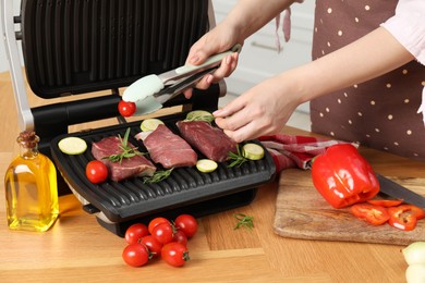 Photo of Woman cooking different products with electric grill at wooden table in kitchen, closeup