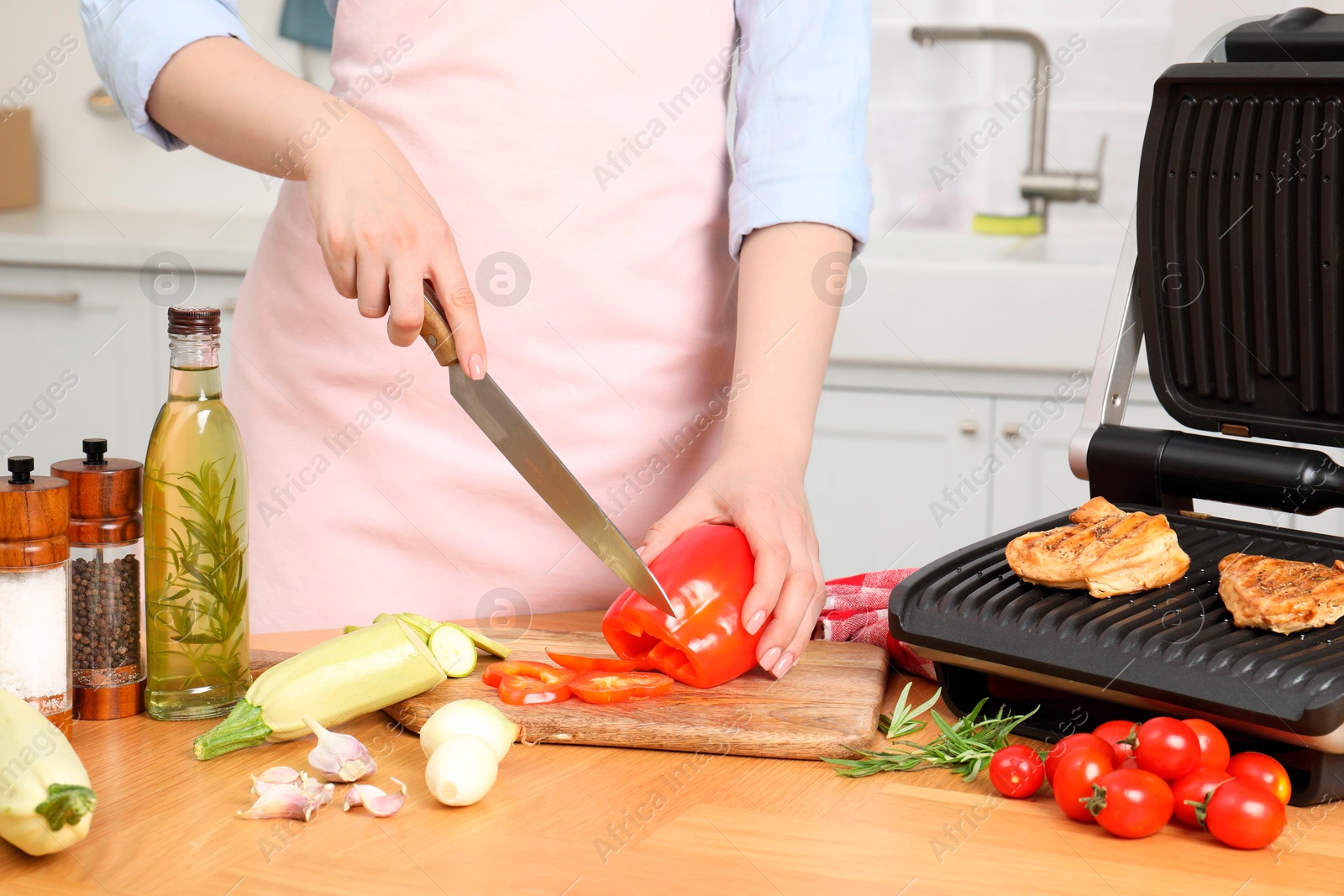 Photo of Woman cooking different products with electric grill at wooden table in kitchen, closeup