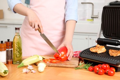 Woman cooking different products with electric grill at wooden table in kitchen, closeup