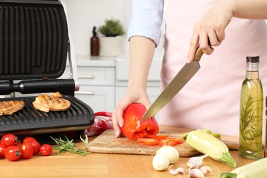 Woman cooking different products with electric grill at wooden table in kitchen, closeup