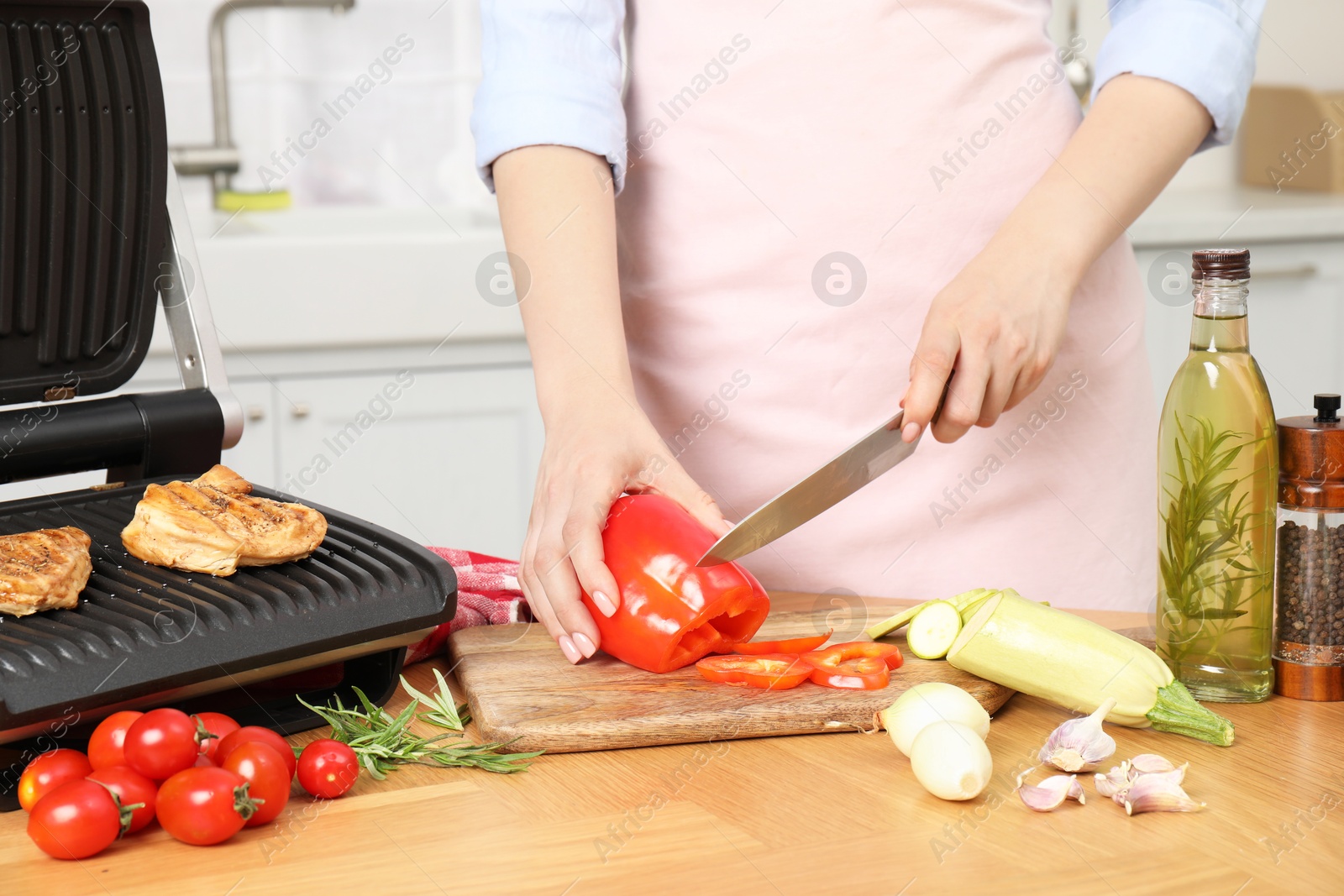 Photo of Woman cooking different products with electric grill at wooden table in kitchen, closeup