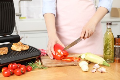 Woman cooking different products with electric grill at wooden table in kitchen, closeup