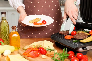 Photo of Woman cooking different products with electric grill at wooden table in kitchen, closeup