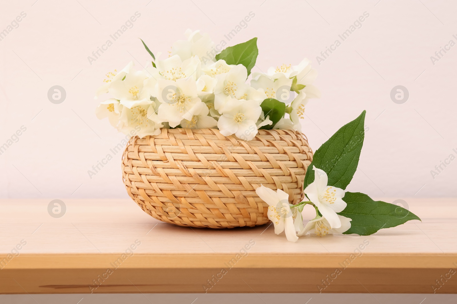 Photo of Beautiful jasmine flowers in wicker basket on wooden table