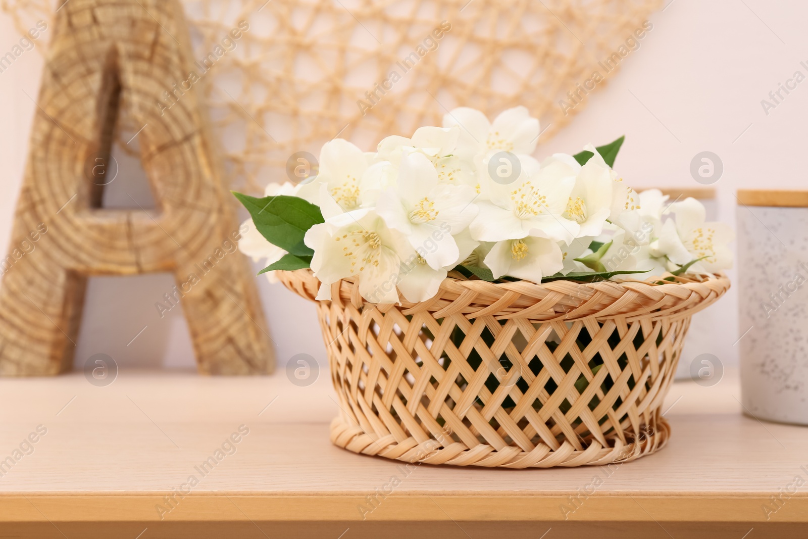 Photo of Beautiful jasmine flowers in wicker basket on wooden table