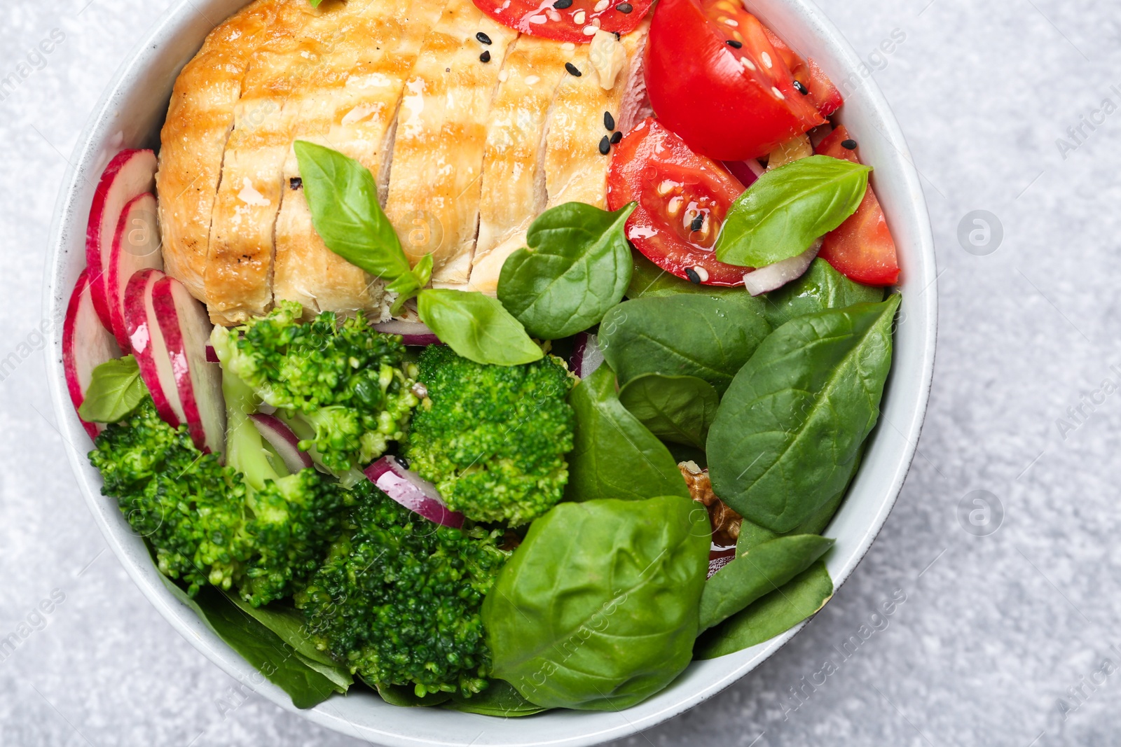 Photo of Healthy meal. Delicious chicken, vegetables and spinach in bowl on light grey table, top view