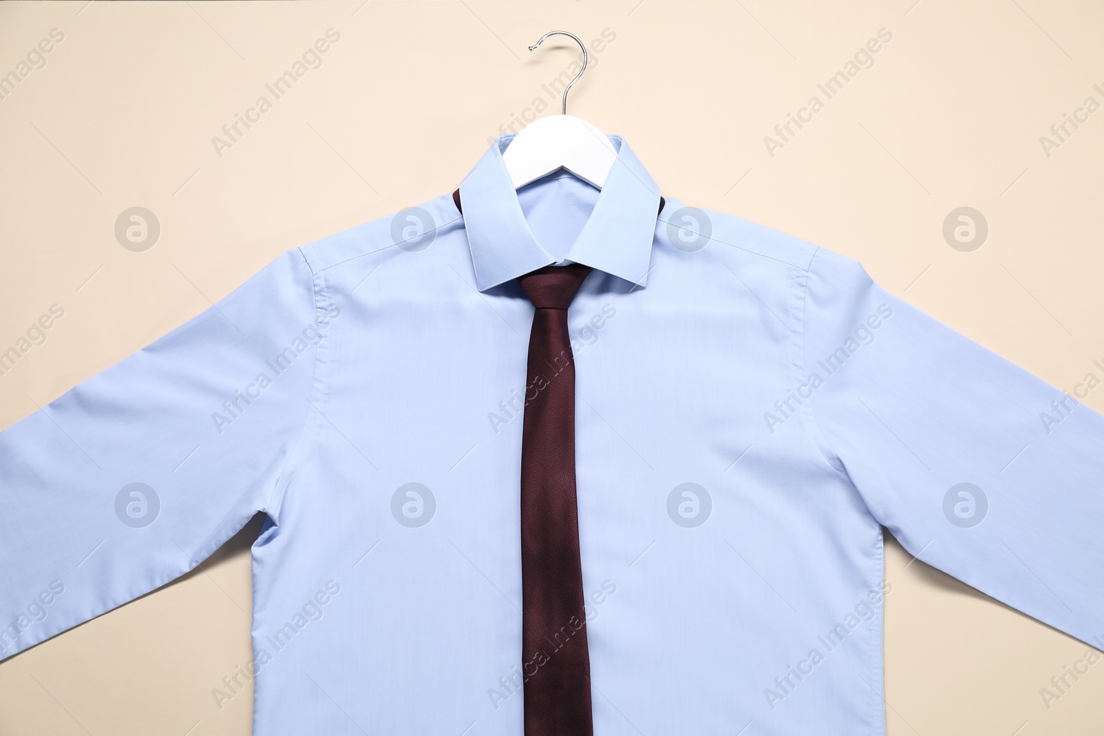 Photo of Hanger with shirt and necktie on beige background, top view