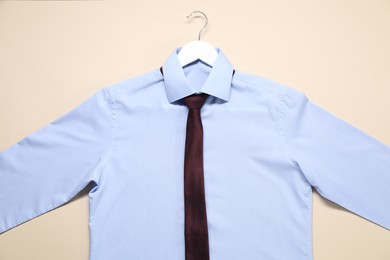 Hanger with shirt and necktie on beige background, top view
