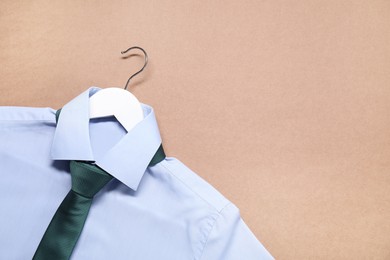 Photo of Hanger with shirt and necktie on beige background, top view. Space for text