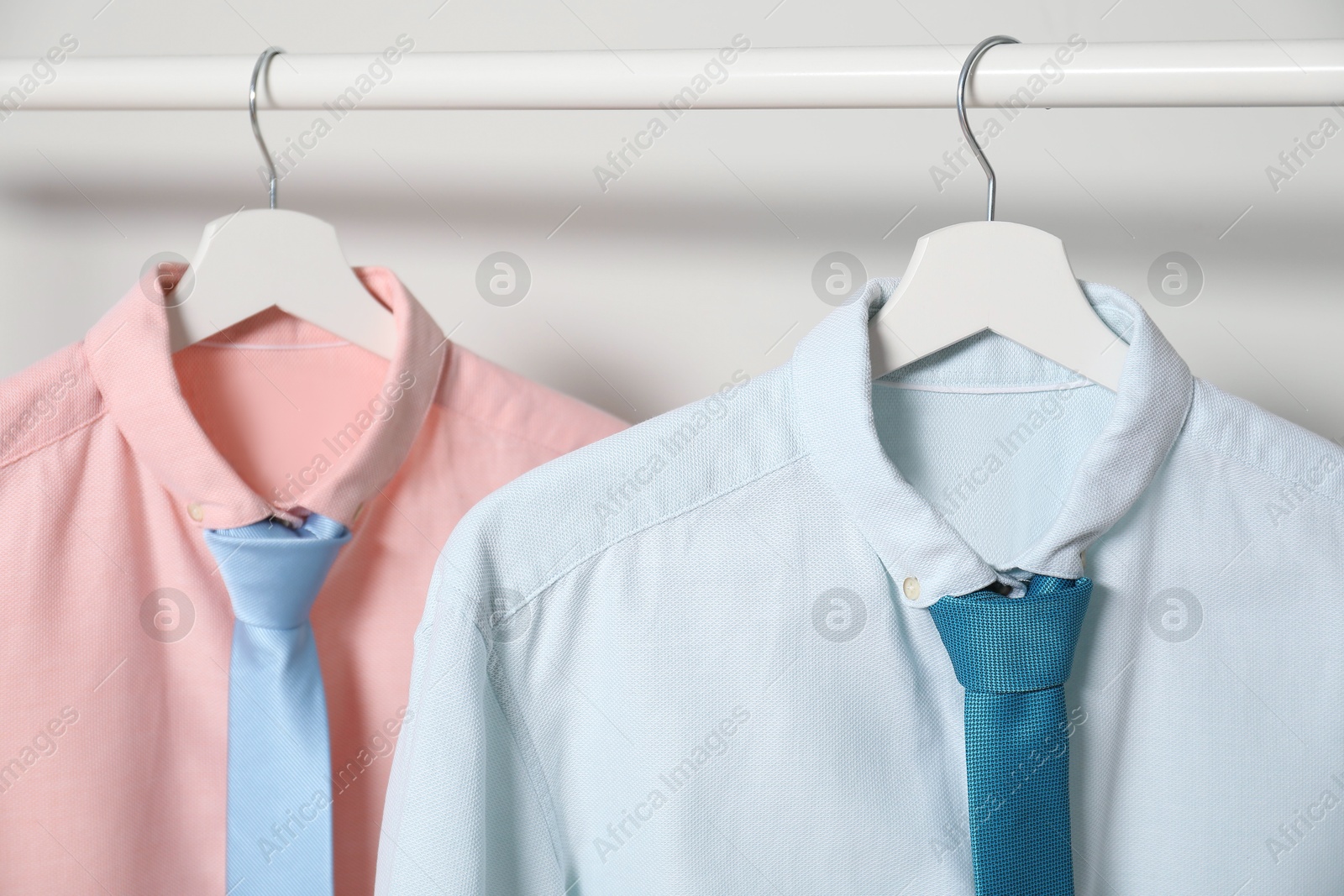 Photo of Hangers with shirts and neckties on light background